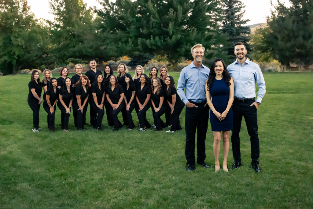 The Personalized Orthodontics staff is standing behind Dr. Kevin, Dr. Kat and Dr. Philip in a grassy park.